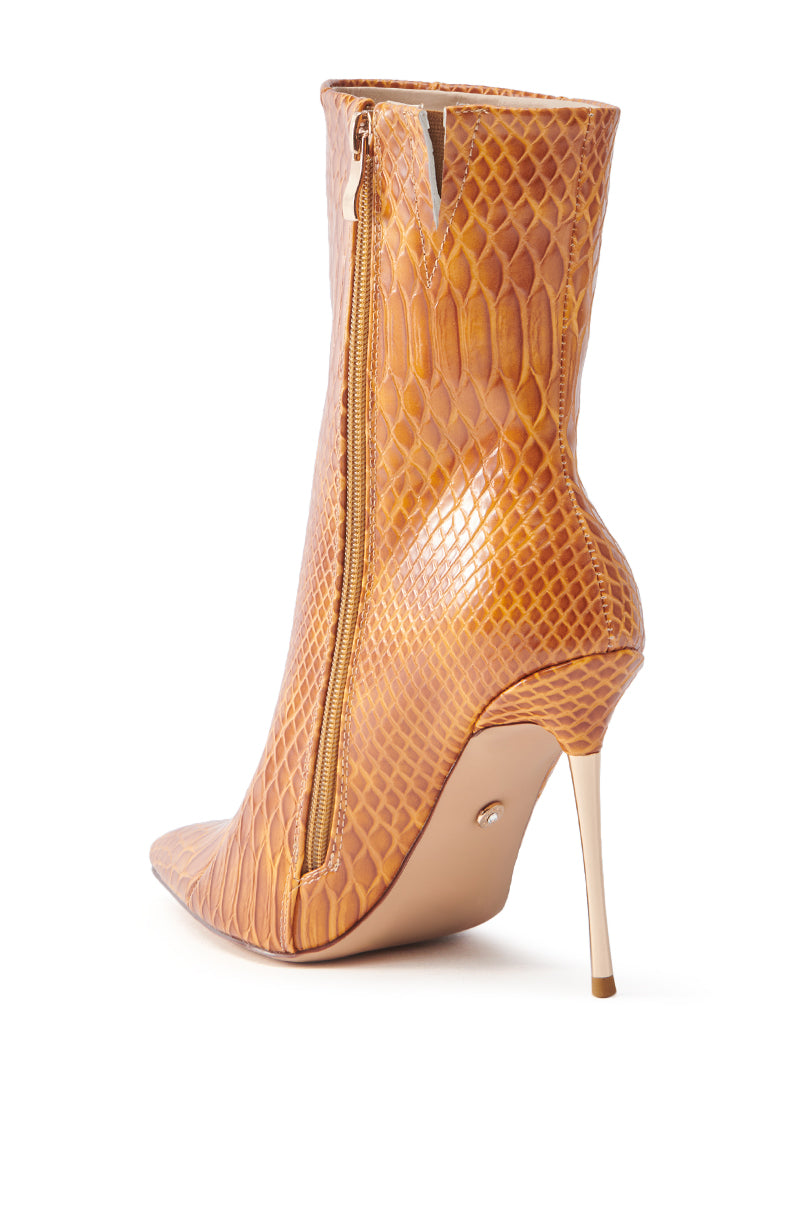 The AZALEA WANG CALEAN ORANGE STILETTO BOOTIE features a high-heeled, ankle-length design with a pointed toe and caramel snakeskin pattern. It has a prominent side zipper, slim stiletto heel, and is crafted from luxurious faux leather.