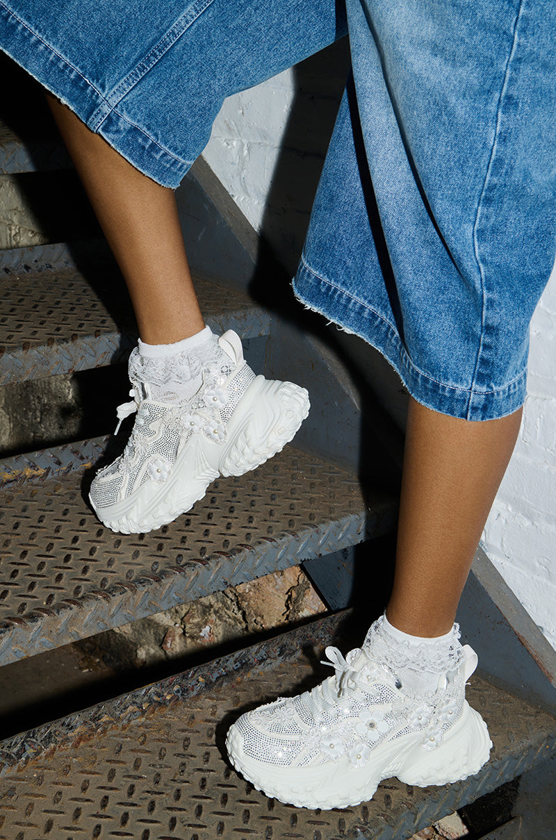 A person wearing the AZALEA WANG CANISH White Embellished Sneakers with textured details and white socks stands on a metal staircase, dressed in blue denim culottes.
