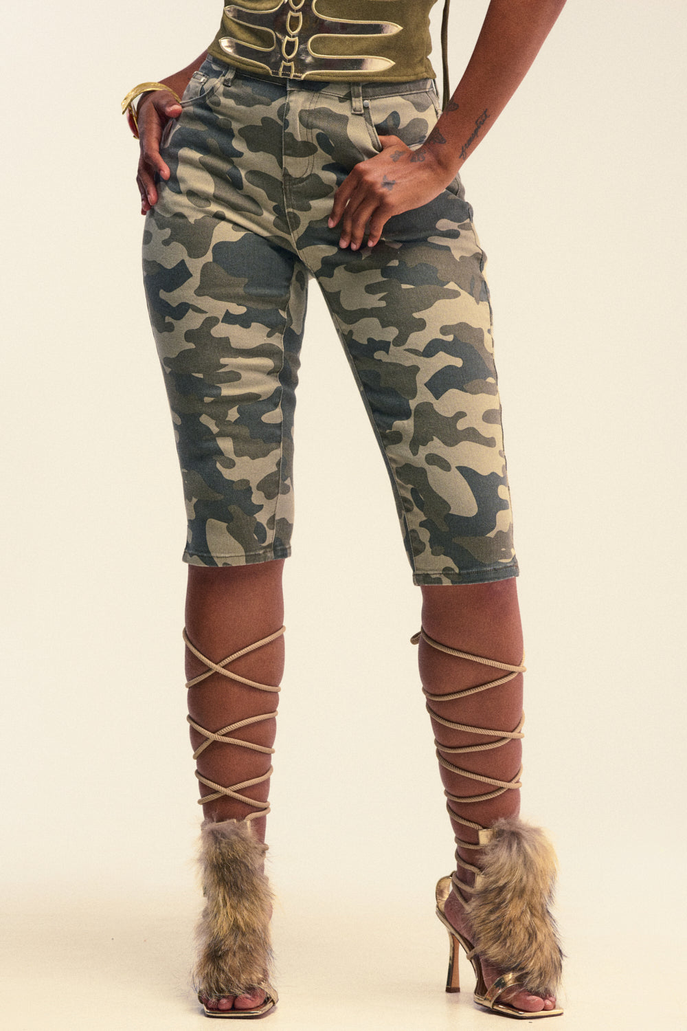 Wearing the I LIKE THIS VIBE CAMO CAPRI—a pair of camo-print, high-rise capri shorts—paired with fur-accented, crisscross lace-up high-heeled sandals and hands casually in pockets, this look makes a bold statement in streetwear style.