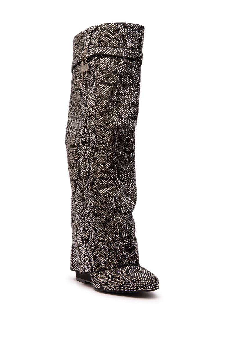 The AZALEA WANG CAPRICORN RHINESTONE SNAKE PATTERN WEDGE FOLD OVER BOOT features a black and white rhinestone snake pattern, pointed toe, wedge heel, and a decorative strap near the top, shown on a white background.