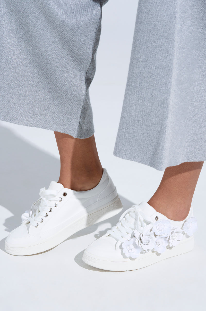 A person wearing light grey wide-leg pants and AZALEA WANG CARNATION WHITE FLAT SNEAKERS stands on a white surface.