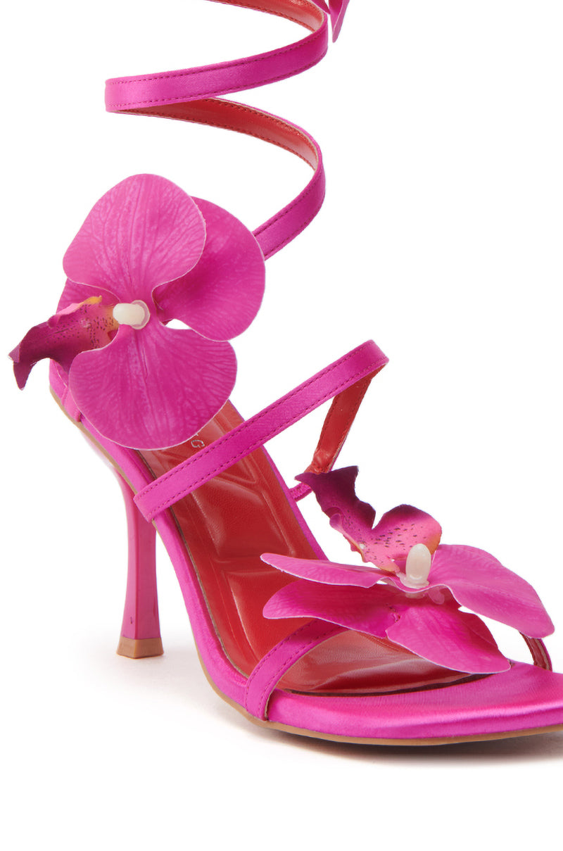 The AZALEA WANG CARRINGTON FUCHSIA FLORAL COIL SANDAL features a satin upper, stiletto heel, ankle strap, and bold pink orchid flower accents on the toe and side.