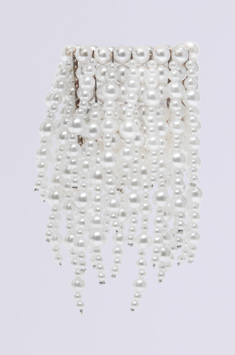 The PEARL VISION STATEMENT BRACELET showcases cascading white bead strands resembling pearls, accented with metallic spacers for elegance. Its layered, flowing design against a plain light background makes it truly eye-catching. 2