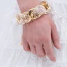 A close-up of a hand wearing the COCO TWEED AND CHAIN BRACELET, featuring chunky gold and fabric links, rests on a white lace-trimmed skirt—perfect for adding luxury vibes to any outfit.
