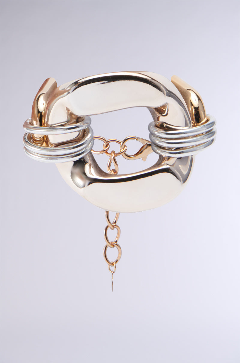 The ULTIMATE BABE BRACELET is a bold metallic blend of gold and silver, featuring interlocking chain pieces. It highlights circular silver rings and includes a dangling chain detail, beautifully adorned with heart-shaped links against a neutral backdrop. 0
