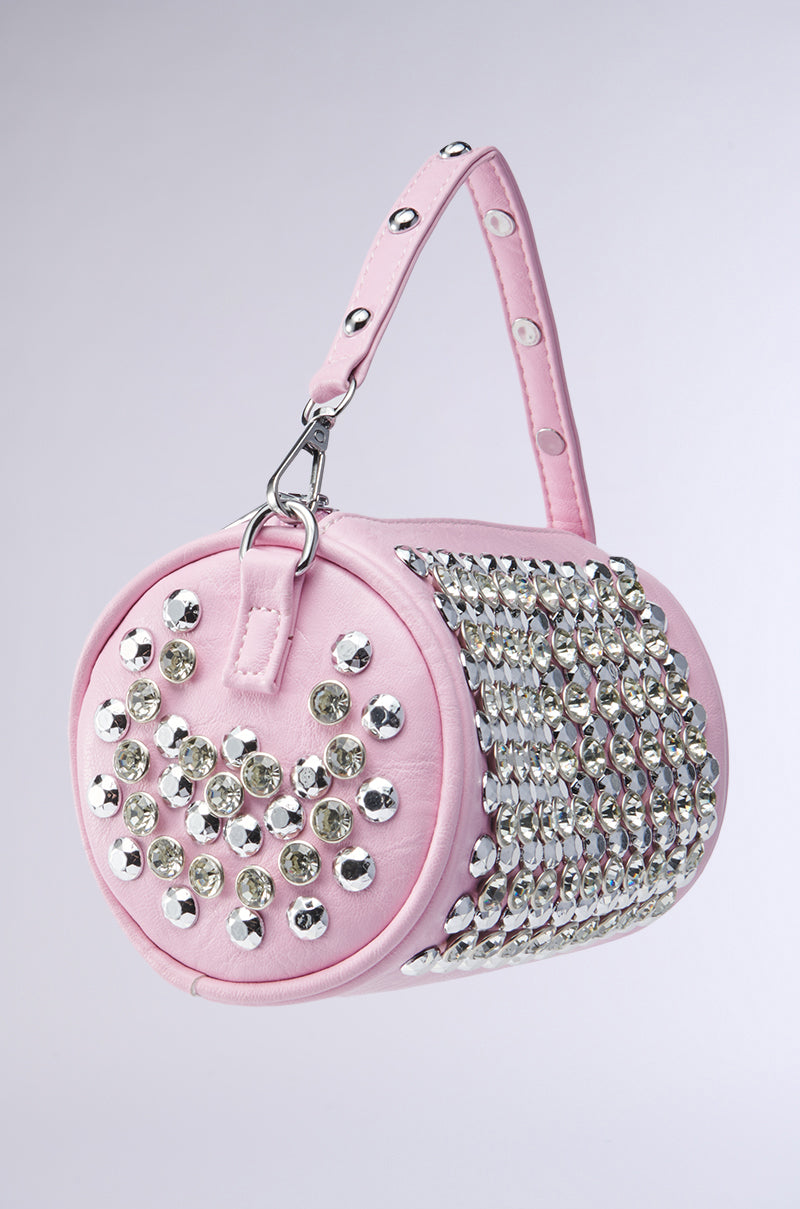 The LUXE LIFESTYLE PURSE is a small, cylindrical pink bag with a handle, featuring large silver studs and rhinestones arranged as a smiley face on one side and in rows on the other.