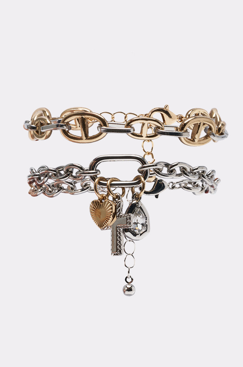 The CHARMED BRACELET SET includes two chain link bracelets: a chunky gold piece and a mixed-metal design adorned with key, heart, sunburst disc, gemstone charms, and dangling beads on a white background.