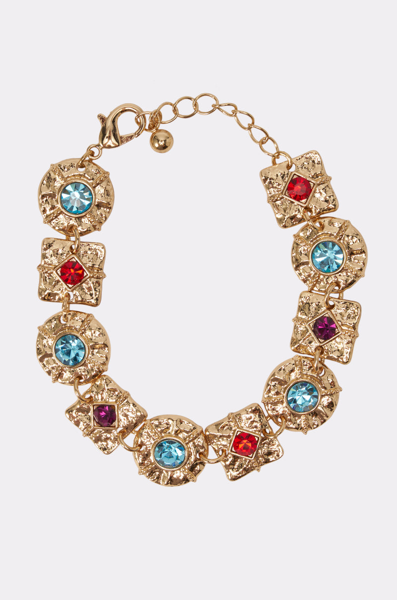 The MULTICOLOR STONE BRACELET showcases elegant styling, featuring alternating blue, red, and purple stones set in textured, star-shaped gold links and finished with an adjustable chain and clasp.