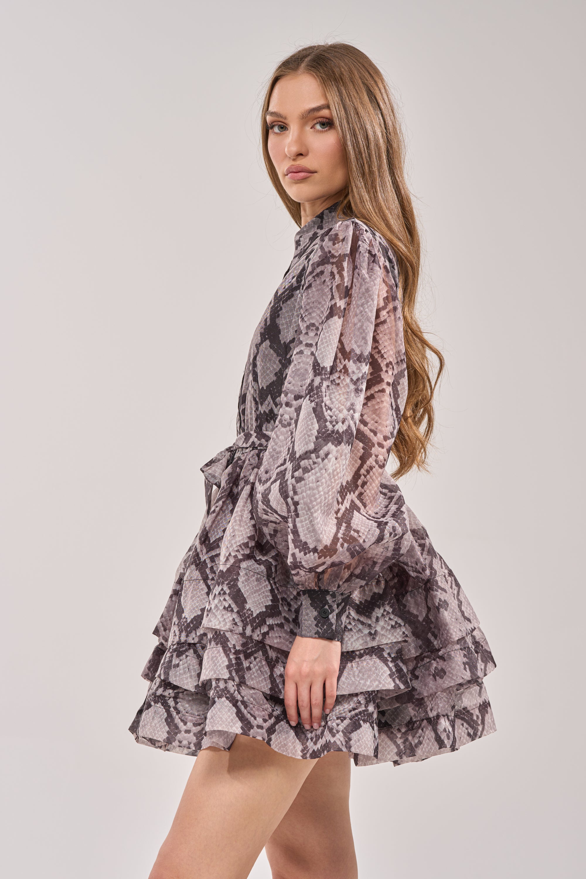 A woman with long brown hair wears the IT GIRL Chiffon Ruffle Mini Dress in Snake, standing sideways and looking at the camera against a plain background. 2