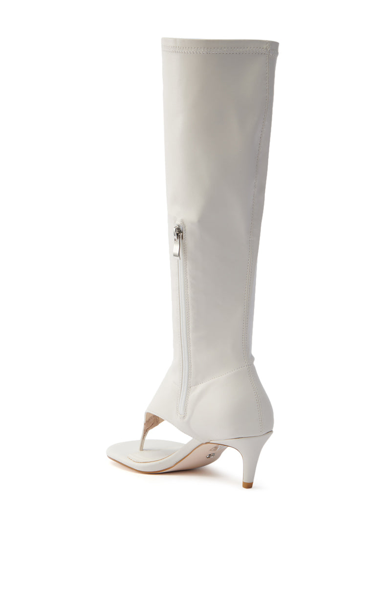 The AZALEA WANG CECILE BONE SANDAL STILETTO is a white, knee-high boot with an open toe and mid-height short stiletto heel. It has a side vertical zipper and a sleek, modern design. The sole is slightly visible and beige in color.
