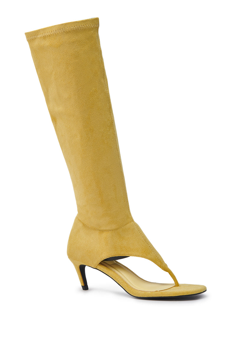 The AZALEA WANG CECILE MUSTARD SANDAL STILETTO features yellow faux suede, an open toe, thong design, mid-height black heel, and a striking knee-high shaft for a bold stiletto look.