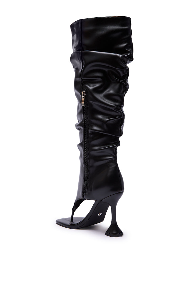 The AZALEA WANG CECILL Black Ruched Upper Gladiator Sandal features a high heel, knee-high ruched black material, side zipper, and open toe thong sandal design, shown against a white background.