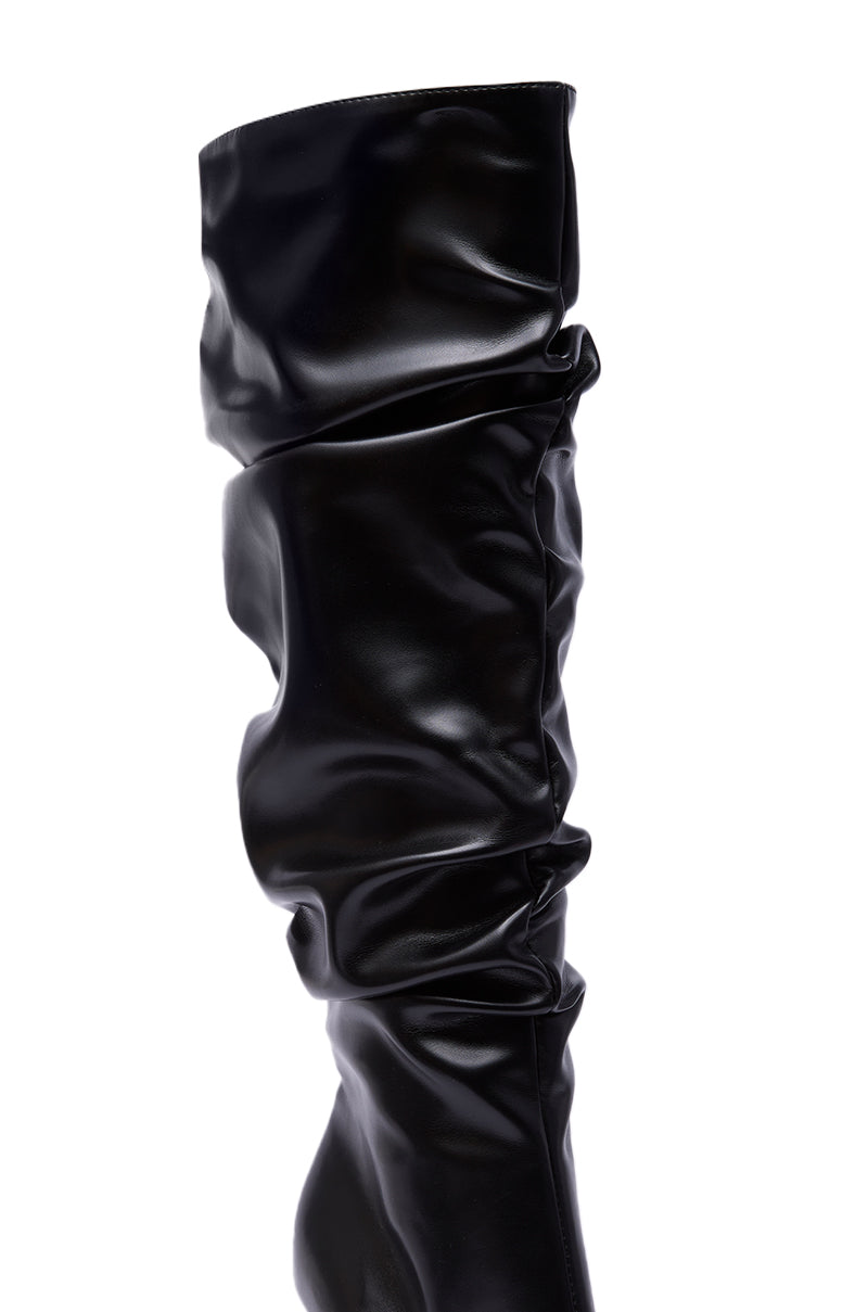 A close-up of the AZALEA WANG CECILL Black Ruched Upper Gladiator Sandal featuring a shiny black finish, ruched detailing on the upper, and a knee-high slouchy silhouette. The background is white.