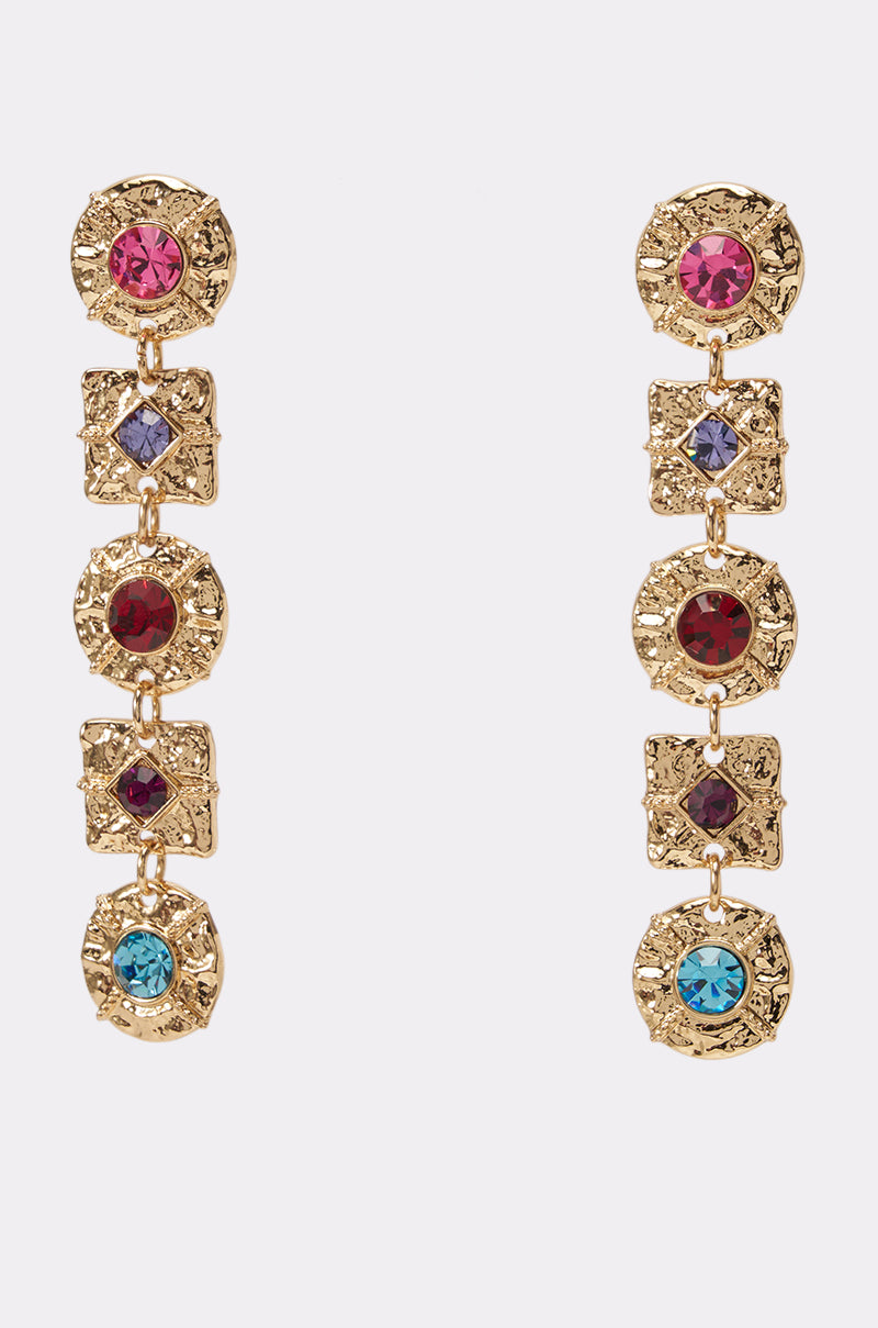 The MULTI-STONE CHANNEL EARRINGS feature two gold drop earrings with alternating round and square segments, each adorned with vibrant red, blue, pink, and purple gemstones. These elegant earrings stand out beautifully against a plain light background and add a sophisticated pop of color to any look.