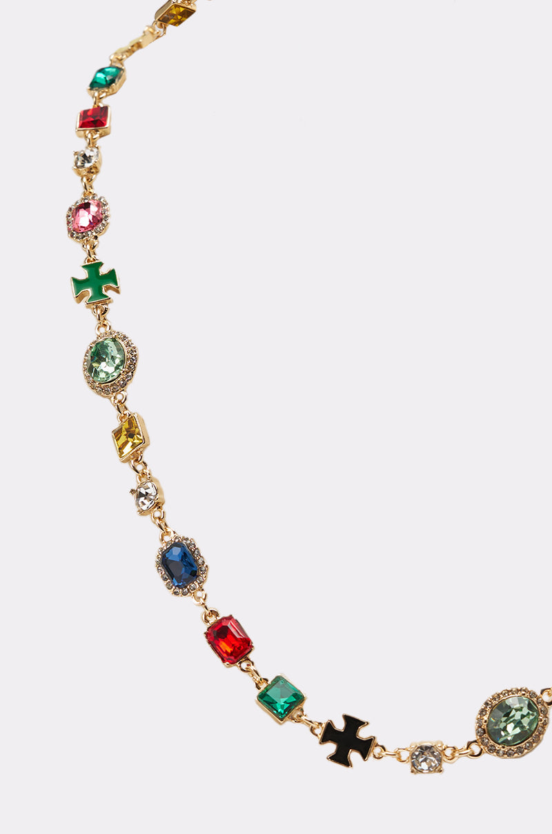 The I AM HER NECKLACE is a gold necklace adorned with colorful gemstones in various shapes and sizes, accented by black cross-shaped charms, shown on a light background. 2