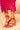 A person stands on a neutral background wearing a ruched bright pink skirt and the AZALEA WANG CELESIA FUCHSIA STILETTO SANDAL in metallic faux leather with comfort cushion insoles and metallic tips.