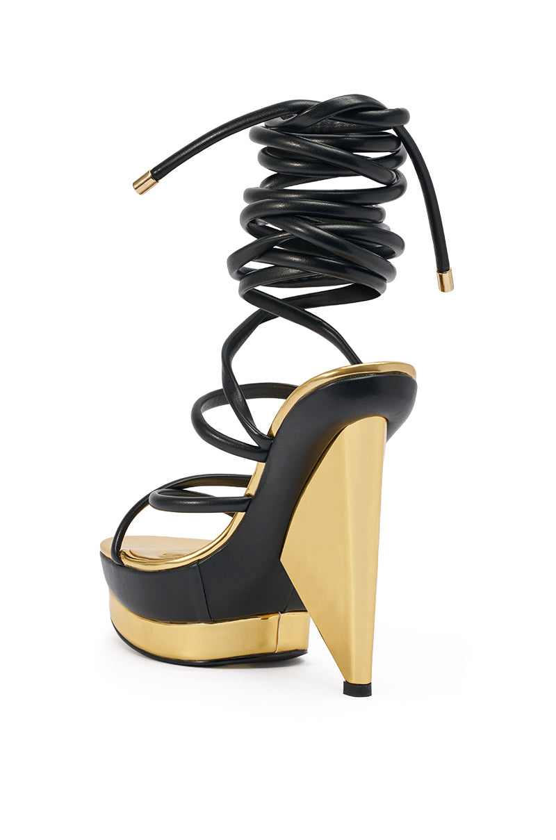 The AKIRA GOLD CELINEA BLACK NOVELTY GOLD HEEL SANDAL features black straps, an ankle wrap that coils upward, a gold platform and sculptural heel, and a glossy modern finish. 6