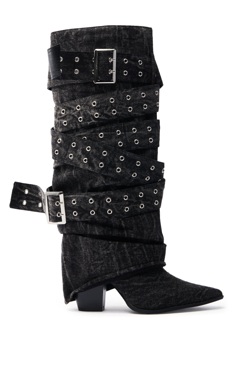 The CENSORED BLACK DENIM BELTED CHUNKY BOOT is a single black denim boot with decorative grommets, two large silver buckles and straps, a mid-calf shaft, pointed toe, and stylish chunky heel.