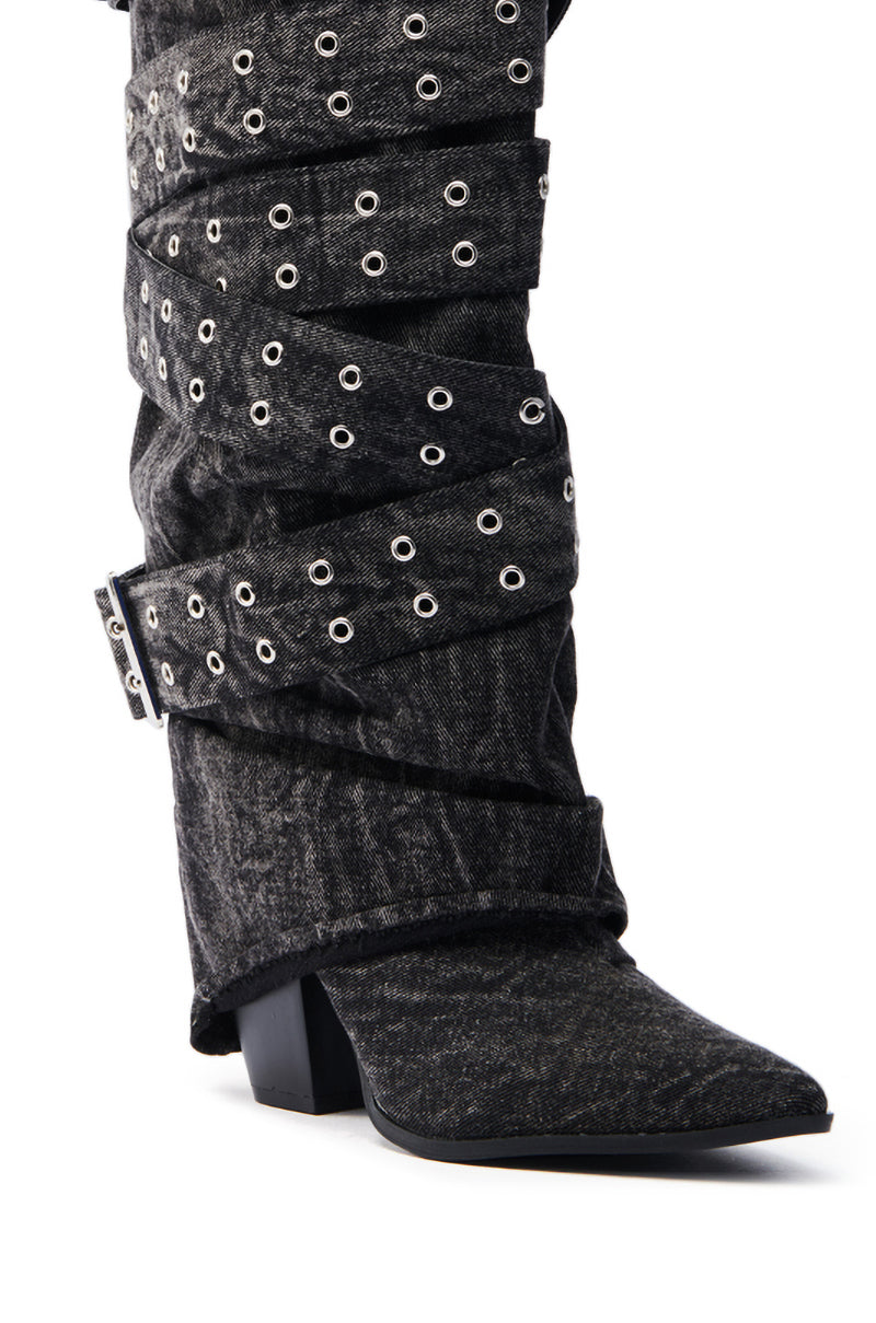 The CENSORED BLACK DENIM BELTED CHUNKY BOOT features a slouchy black denim design with a pointed toe, mid-height chunky heel, decorative silver grommets, a wide buckle strap, and mid-calf shaft for an edgy fashion-forward look.