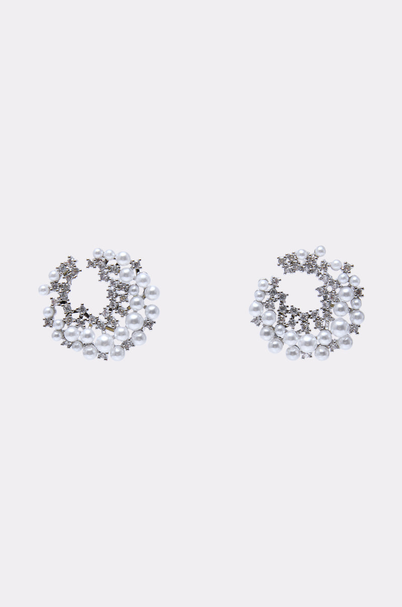 The TRISH EARRING is a pair of circular statement earrings with small white faux pearls and silver crystals in a clustered open-hoop design, shown on a plain white background. 0