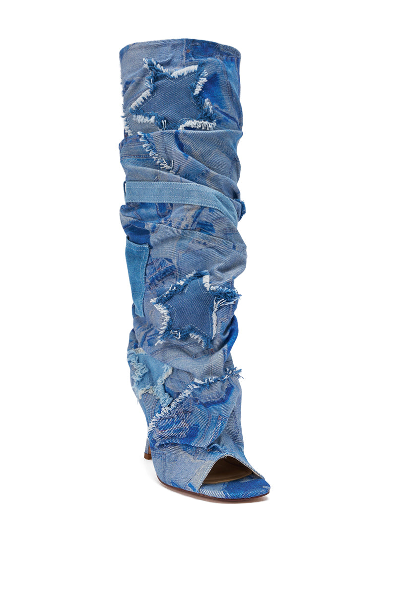 The AZALEA WANG CHAITRA DENIM OPEN TOE BOOT is a knee-high slouch boot with a stiletto heel, made from distressed blue denim. It features frayed edges, star-shaped patches, and a peep-toe design against a white background.