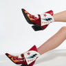 Two legs in AZALEA WANG CHANNING MULTI WESTERN BOOTIE with red and white faux leather, stars, and lightning bolt designs stand gracefully against a plain white background. These booties have angled chunky heels and studded details.