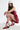 A woman crouches against a white background, wearing a red sequined dress, the AZALEA WANG CHANNING MULTI WESTERN BOOTIE with bold designs, long dark hair, and a white bandana.
