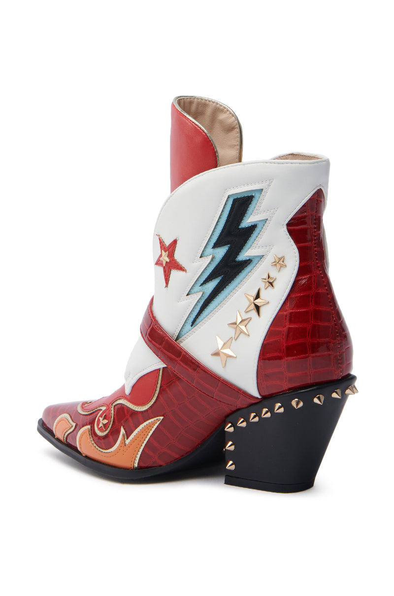 The AZALEA WANG CHANNING MULTI WESTERN BOOTIE is a stylish pointed toe boot with an angled heel, featuring a red crocodile texture, white upper with a black lightning bolt, red star, and gold stars. Gold cone studs adorn the heel's back edge for added flair.