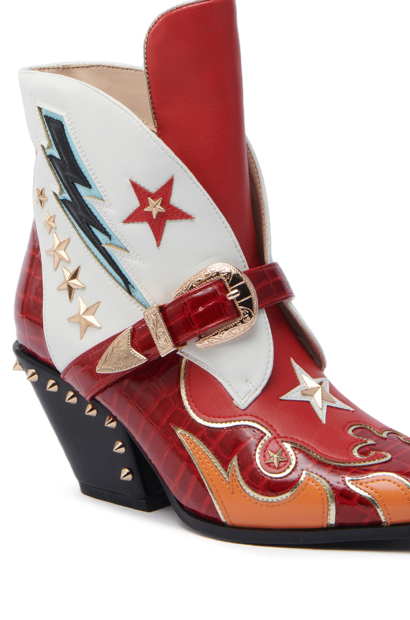 The AZALEA WANG CHANNING MULTI WESTERN BOOTIE features a vibrant pointed toe design with red, white, and orange leather panels. Adorned with star and lightning bolt motifs, it includes a decorative gold buckle and is finished with a chunky black heel embellished with gold studs.