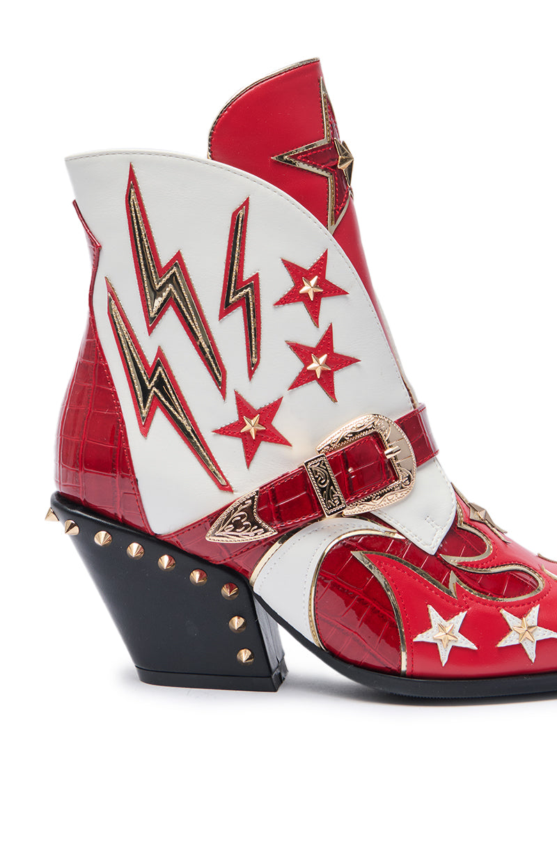 The AZALEA WANG CHANNY MULTI BOOTIE GRAPHIC WESTERN WITH STUDS is a bold red and white bootie featuring gold lightning bolts, stars, a decorative buckle, gold studs, and a uniquely angled chunky heel.
