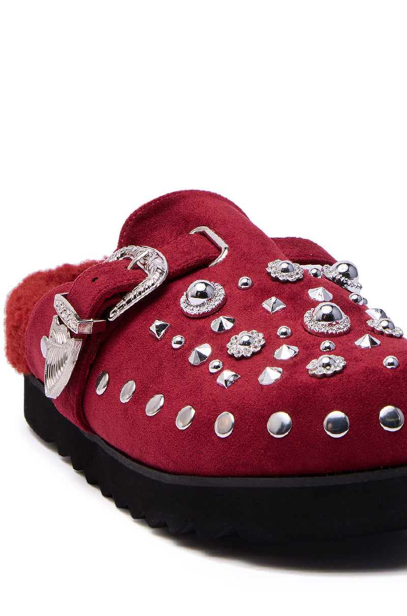 The AZALEA WANG CHATTER BURGUNDY FUR SLIP ON CLOG features faux suede, a large Western-style buckle, silver studs on the upper, and sits on a sleek black sole.