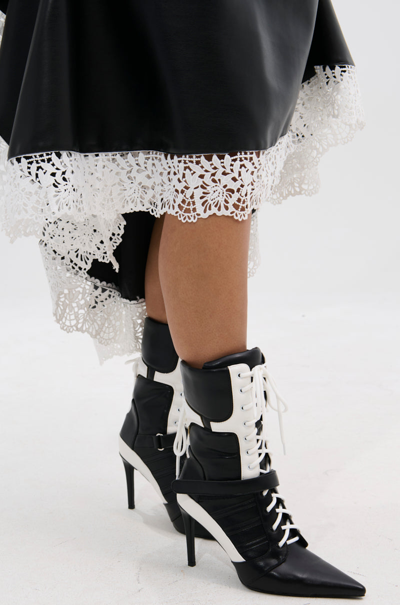 A person wearing the AZALEA WANG CHAUSIKU BLACK SPORTY BOOTIE stands on a light surface, paired with a black skirt featuring a white lace hem.