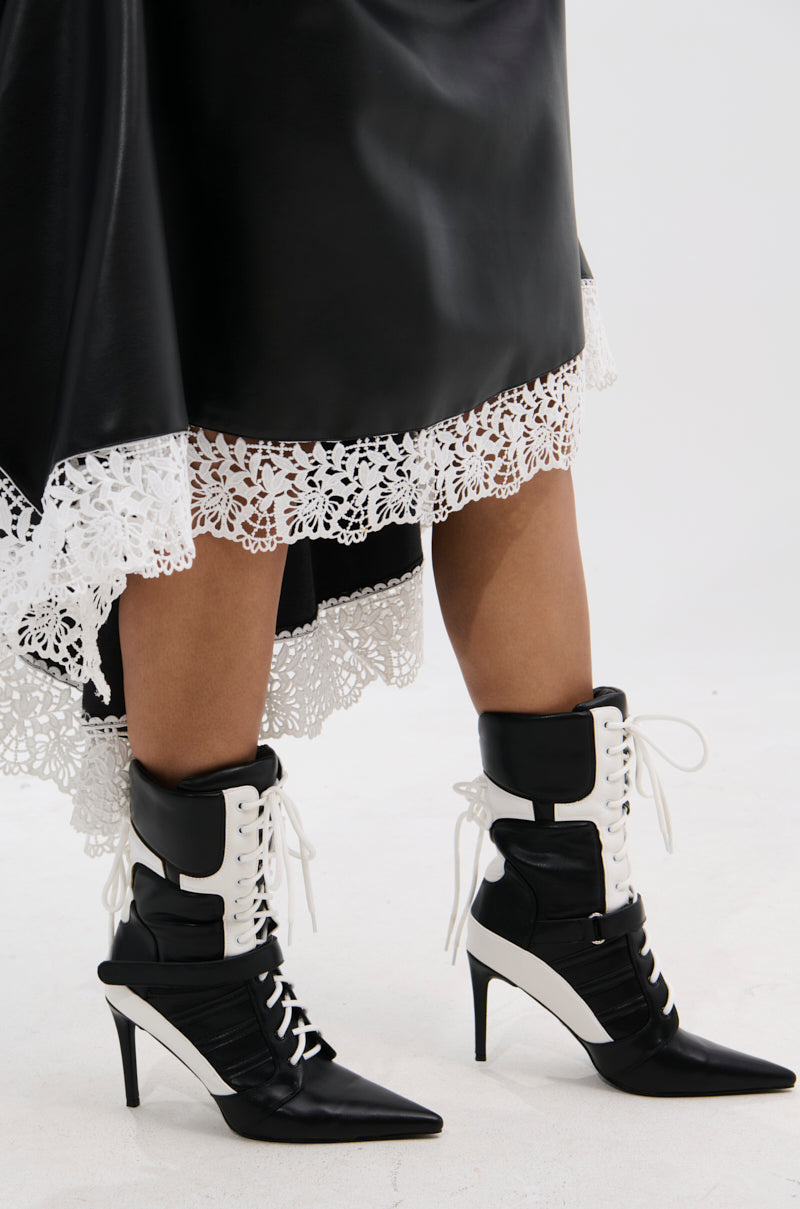 A person stands against a plain light background wearing a black faux leather skirt with white lace trim and the AZALEA WANG CHAUSIKU BLACK SPORTY BOOTIE.