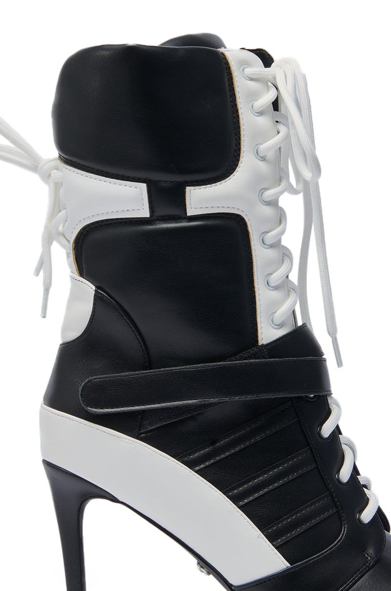 A close-up of the AZALEA WANG CHAUSIKU BLACK SPORTY BOOTIE, a black and white high-heeled sneaker boot featuring a stiletto heel, white laces, padded ankle collar, and front strap for a sporty yet fashionable look.