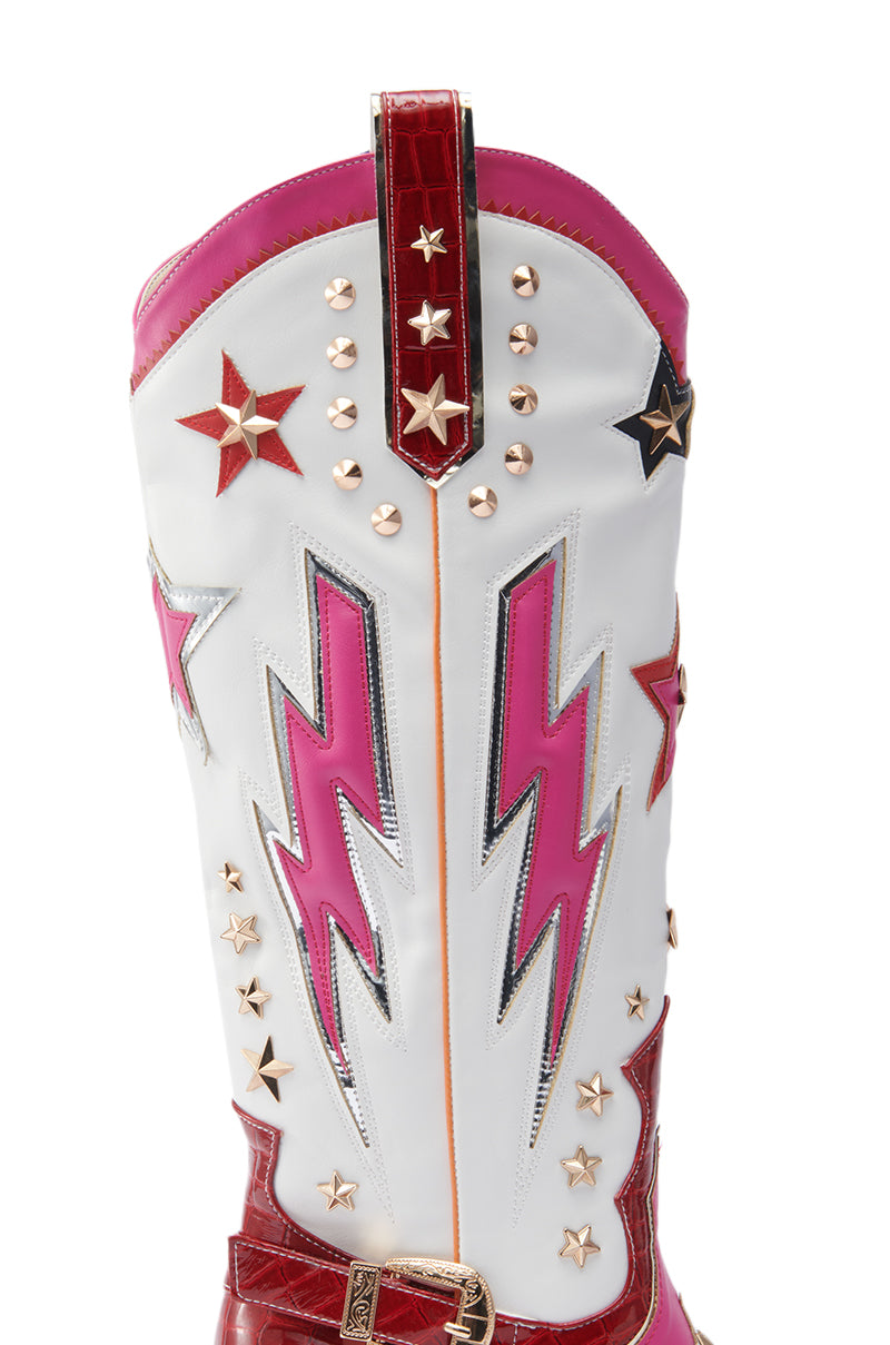 A close-up of the AZALEA WANG CHEONA RED MULTI WESTERN BOOT, a white and red knee-high faux leather boot with pink lightning bolts, gold and black star studs, and metallic accents.