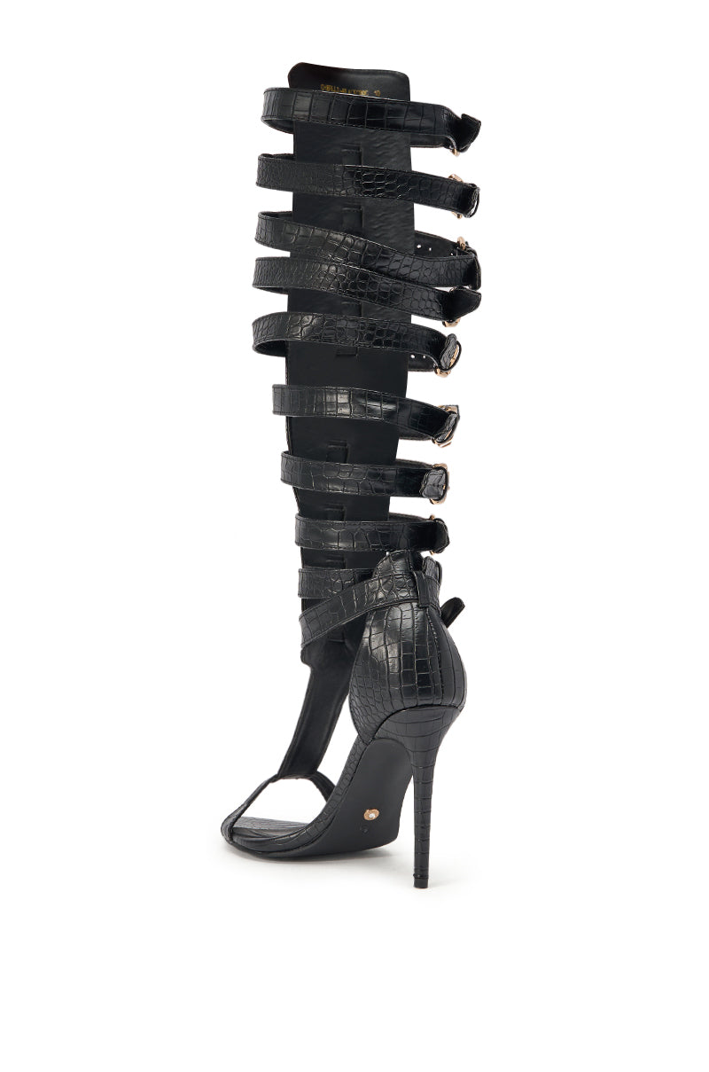 The AZALEA WANG CHERLLI BLACK CROC OVER THE KNEE SANDAL is a bold, knee-high cage sandal with black croc-embossed faux leather, an open toe, stiletto heel, and multiple buckle straps that reach just below the knee. 5