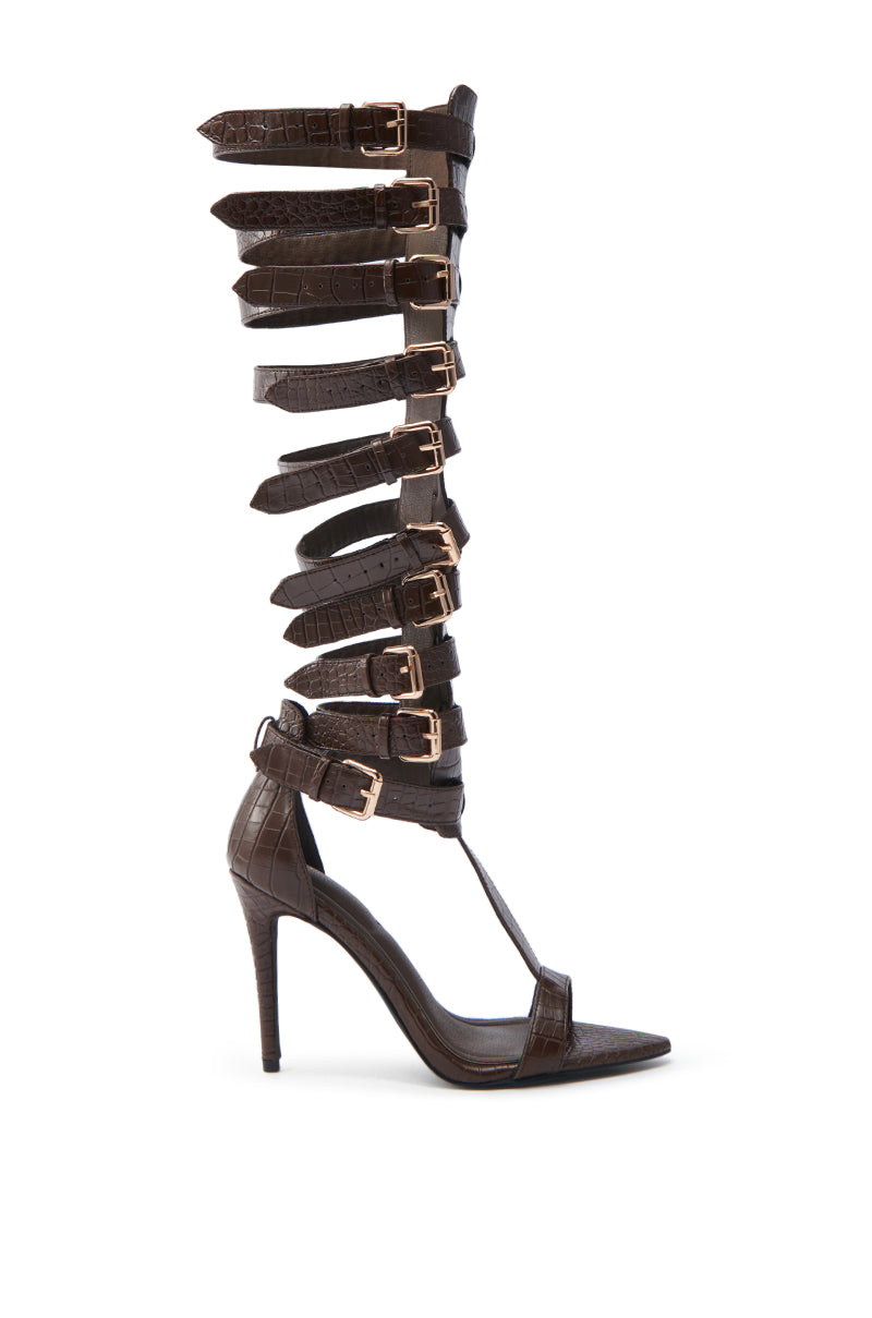 The AZALEA WANG CHERELLI BROWN CROC OVER THE KNEE SANDAL is a stunning open-toe gladiator with multiple adjustable straps, crafted from dark brown croc-embossed leather. It features a textured finish and a sleek stiletto heel.