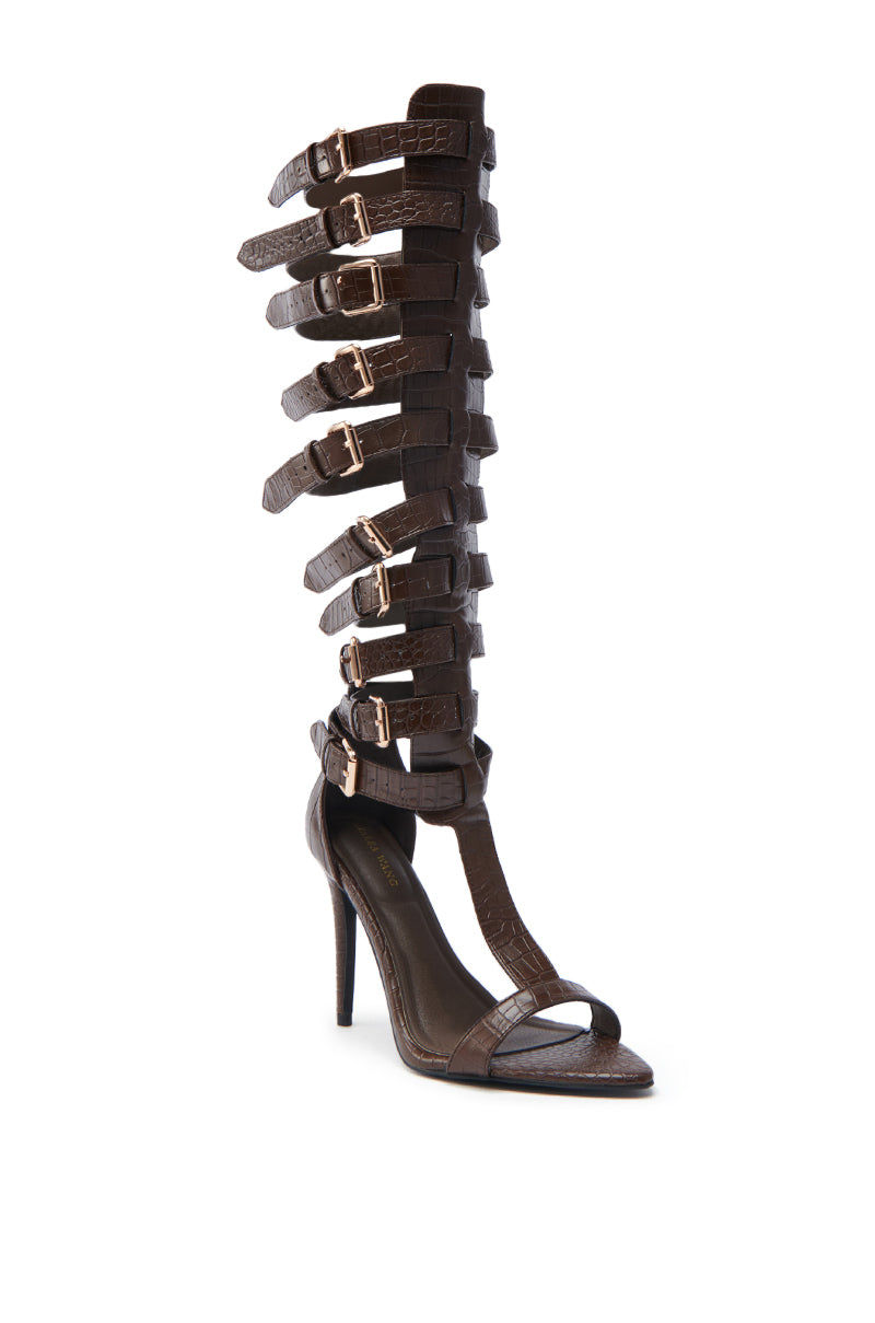 The AZALEA WANG CHERELLI BROWN CROC OVER THE KNEE SANDAL is a chic gladiator design with faux croc-embossed leather straps, gold buckles, extending knee-high, and featuring a sophisticated stiletto heel.