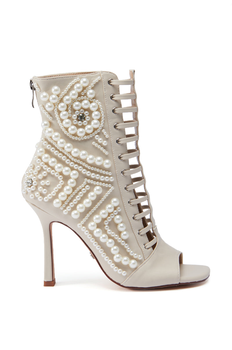 The AZALEA WANG CHIPPER BONE BOOTIE WITH PEARL EMBELLISHMENT is a cream-colored faux leather bootie featuring a peep toe and intricate pearl decorations covering its surface. This stunning stiletto heel boasts a lace-up design and includes a convenient back zipper. 3