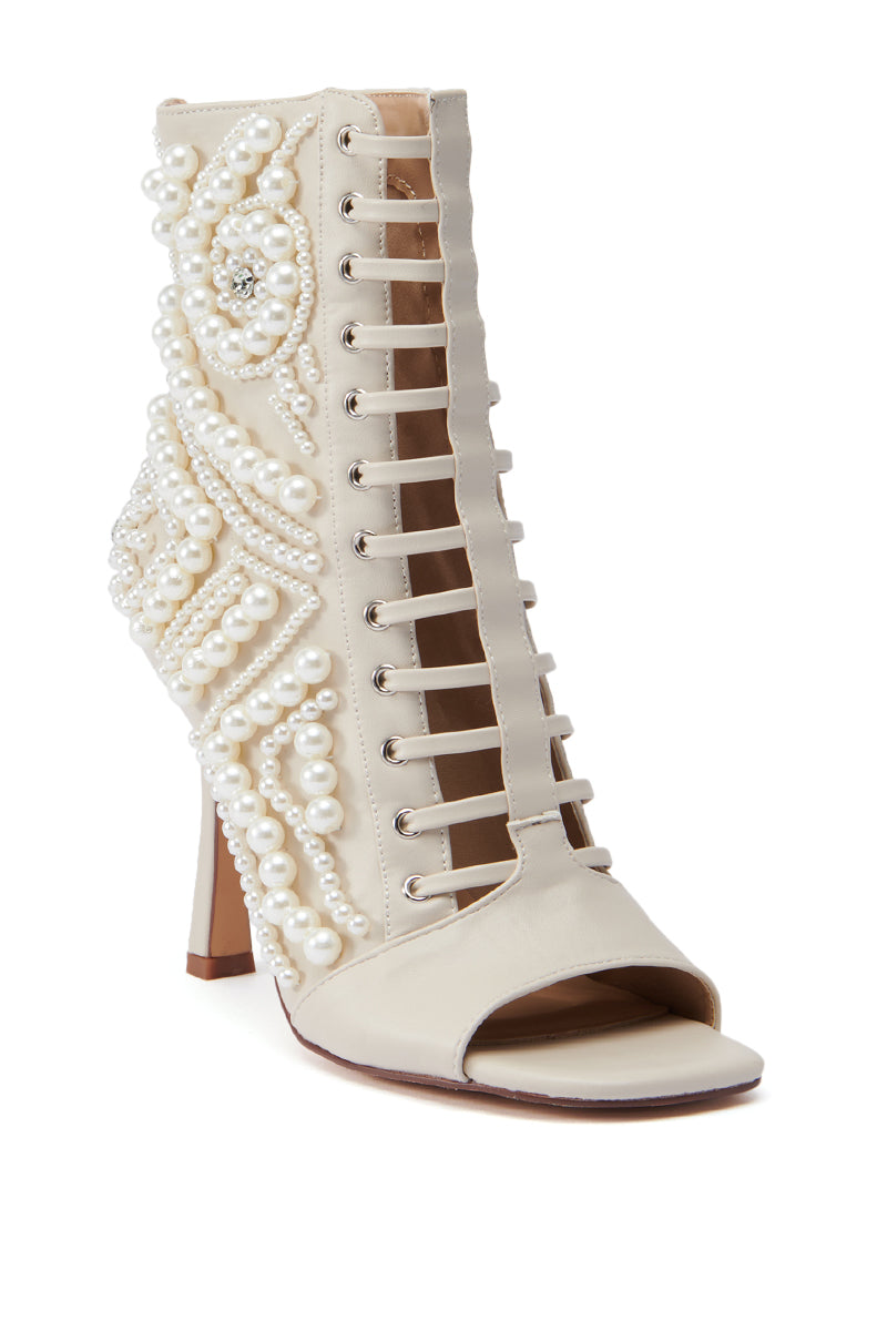 Introducing the AZALEA WANG Chipper Bone Bootie, an elegant high-heeled shoe crafted from creamy white satin-like material. This faux leather bootie features a sophisticated open-toed design adorned with intricate pearl embellishments, a lace-up front, and a tapered stiletto heel for added allure. 4