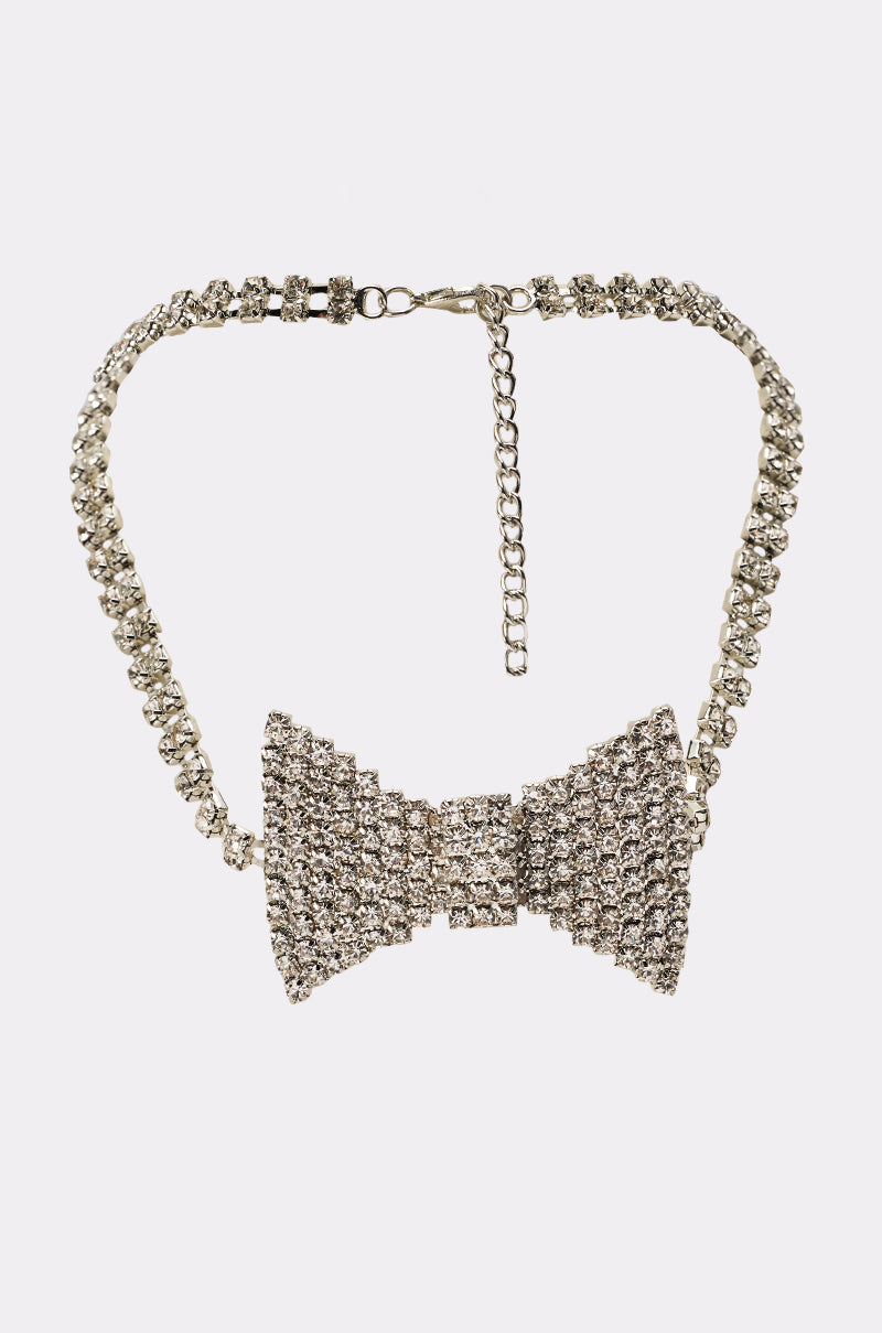 The DAPPER CHOKER NECKLACE features a silver rhinestone chain and a sparkling large bow pendant at the center, showcased on a plain white background. 0