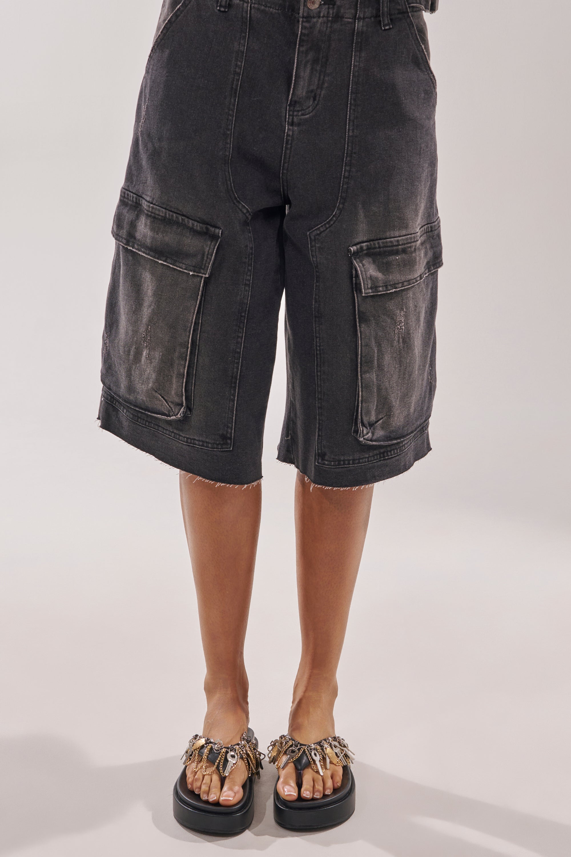 A person in long black cargo shorts with large pockets and raw hems stands against a plain background, paired with AKIRA GOLD CHRISTEN BLACK KEY EMBELLISHED NOVELTY PLATFORM SANDALS featuring bold key details. 2