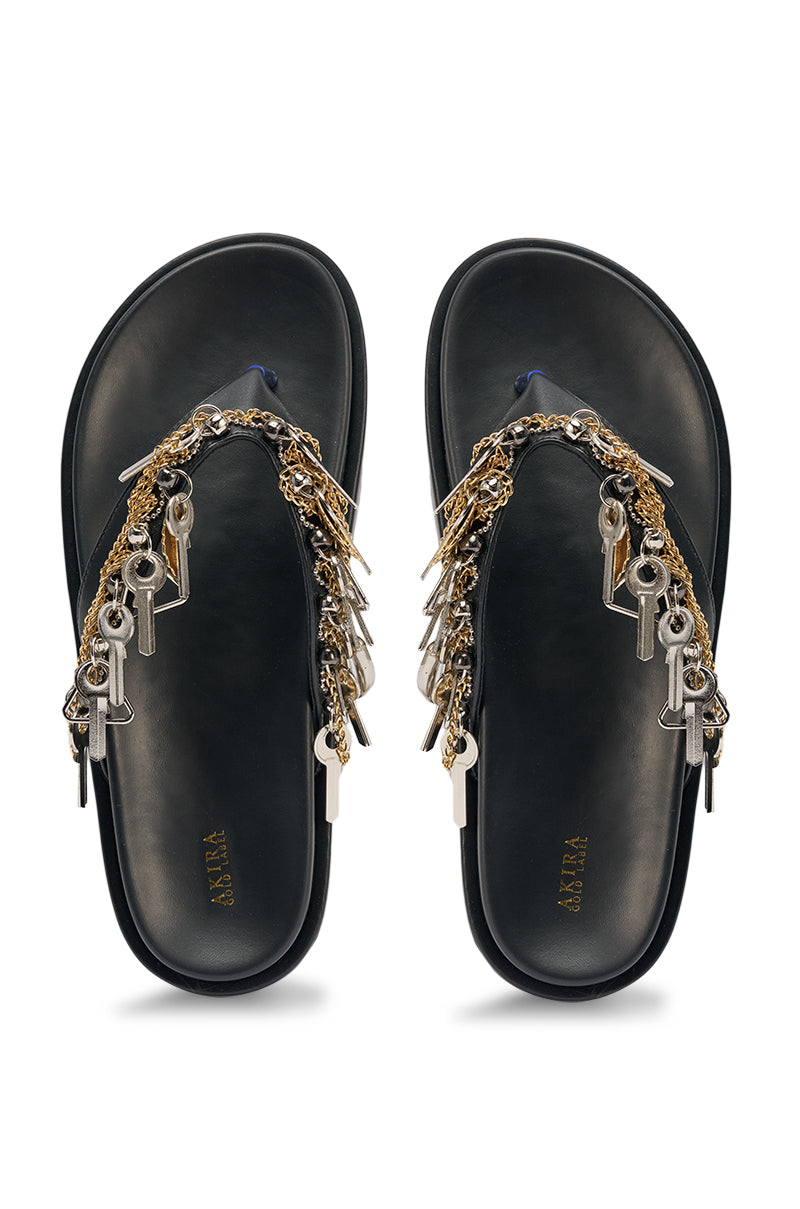 The AKIRA GOLD CHRISTEN BLACK KEY EMBELLISHED NOVELTY PLATFORM SANDAL is a black faux leather slide with a chunky platform sole, featuring silver and gold key and chain charms on the straps. 4