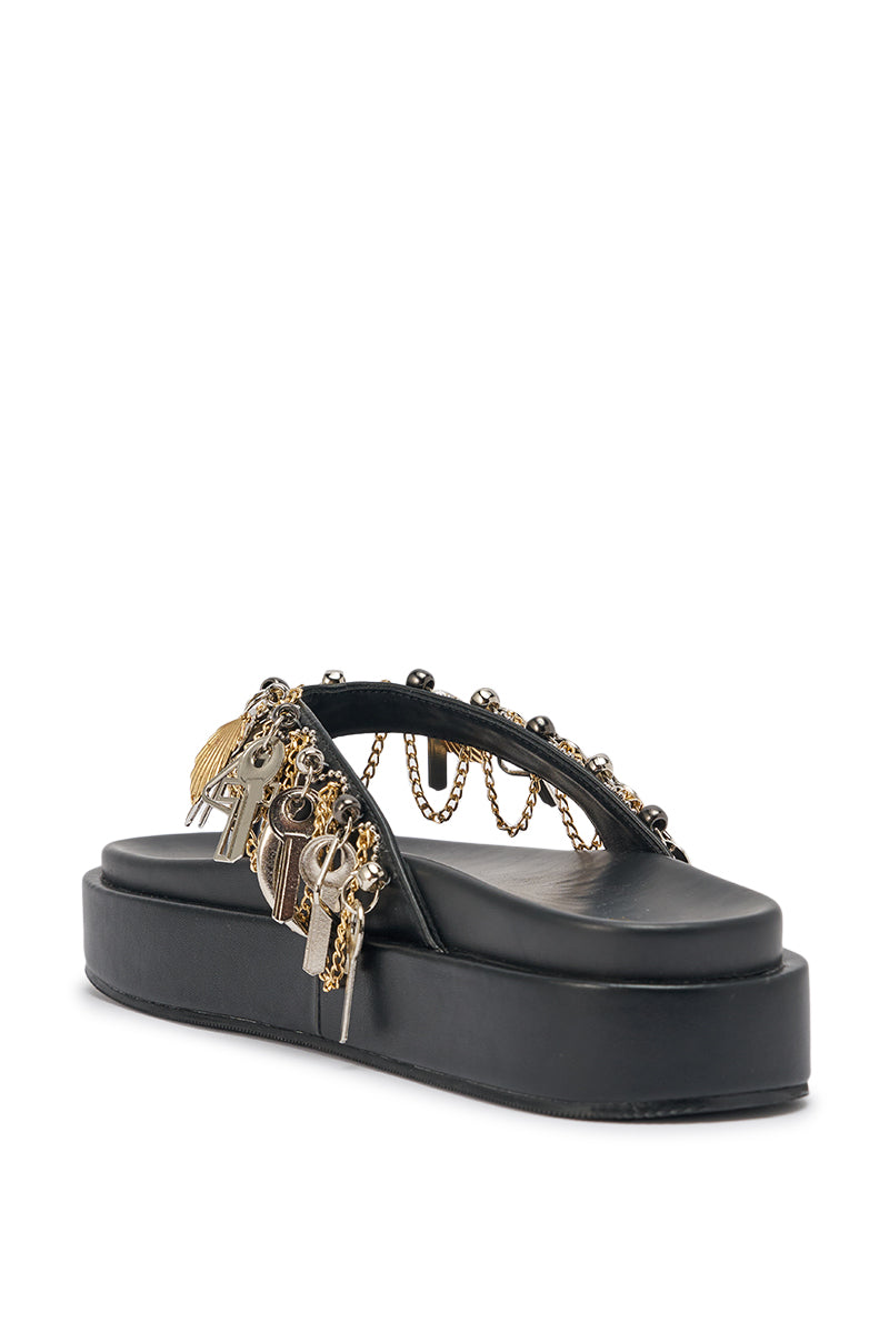The AKIRA GOLD CHRISTEN BLACK KEY EMBELLISHED NOVELTY PLATFORM SANDAL is a black faux leather sandal with a chunky platform sole, detailed with gold & silver charms, chains, and decorative studs on the straps. 7