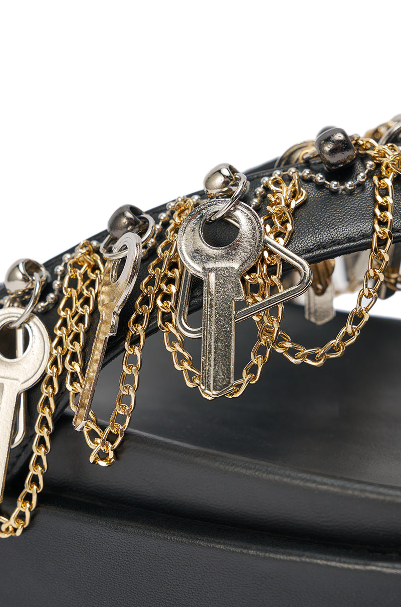 Close-up of the AKIRA GOLD CHRISTEN BLACK KEY EMBELLISHED NOVELTY PLATFORM SANDAL, featuring chunky platform soles and bold gold chain with metal key accents on a black leather handle, with a softly blurred background. 8