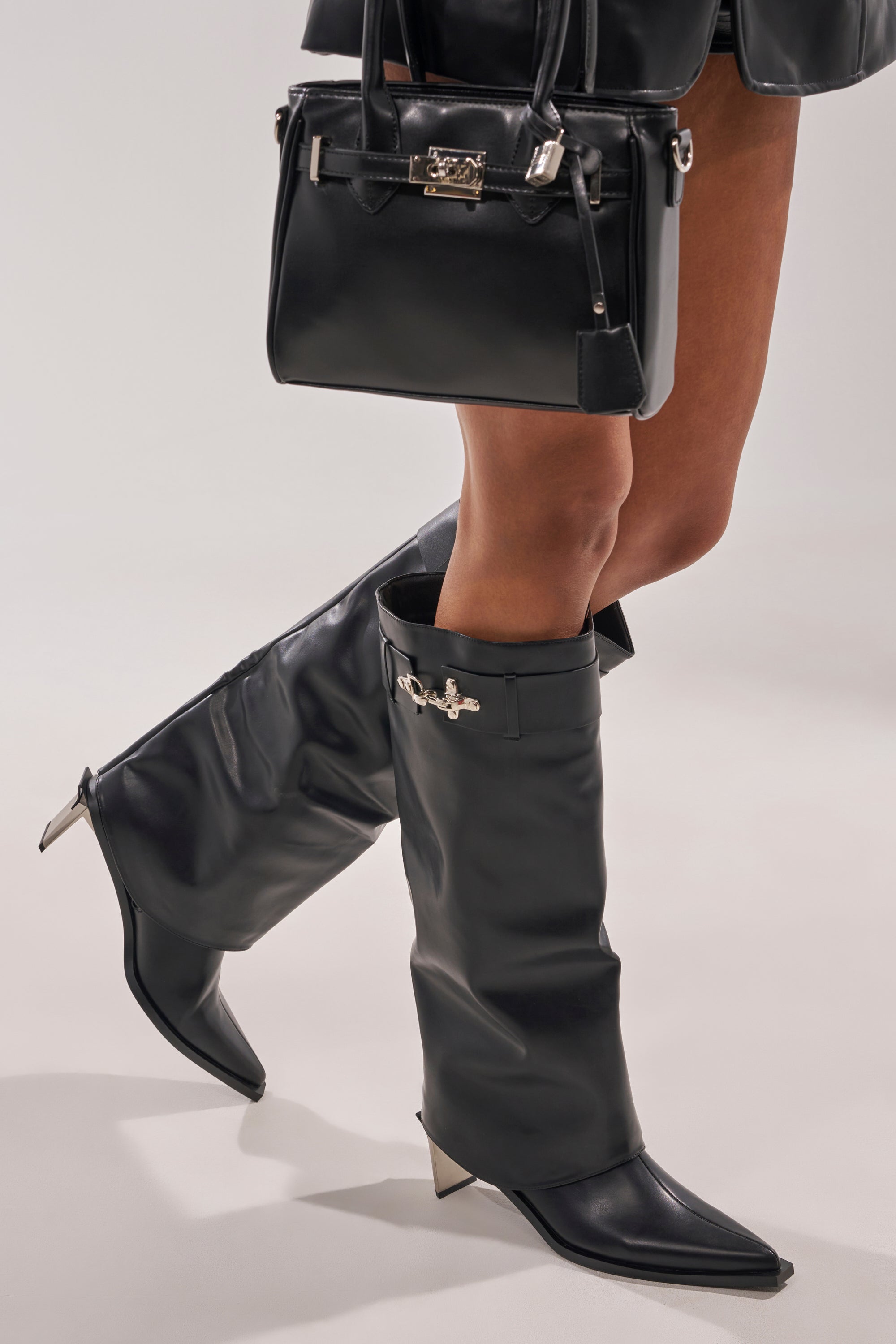 Wearing the AZALEA WANG CHRONO BLACK METAL HEEL BOOT—pointed toe, knee-high with silver accents—styled with a black leather handbag and a black mini skirt. 0