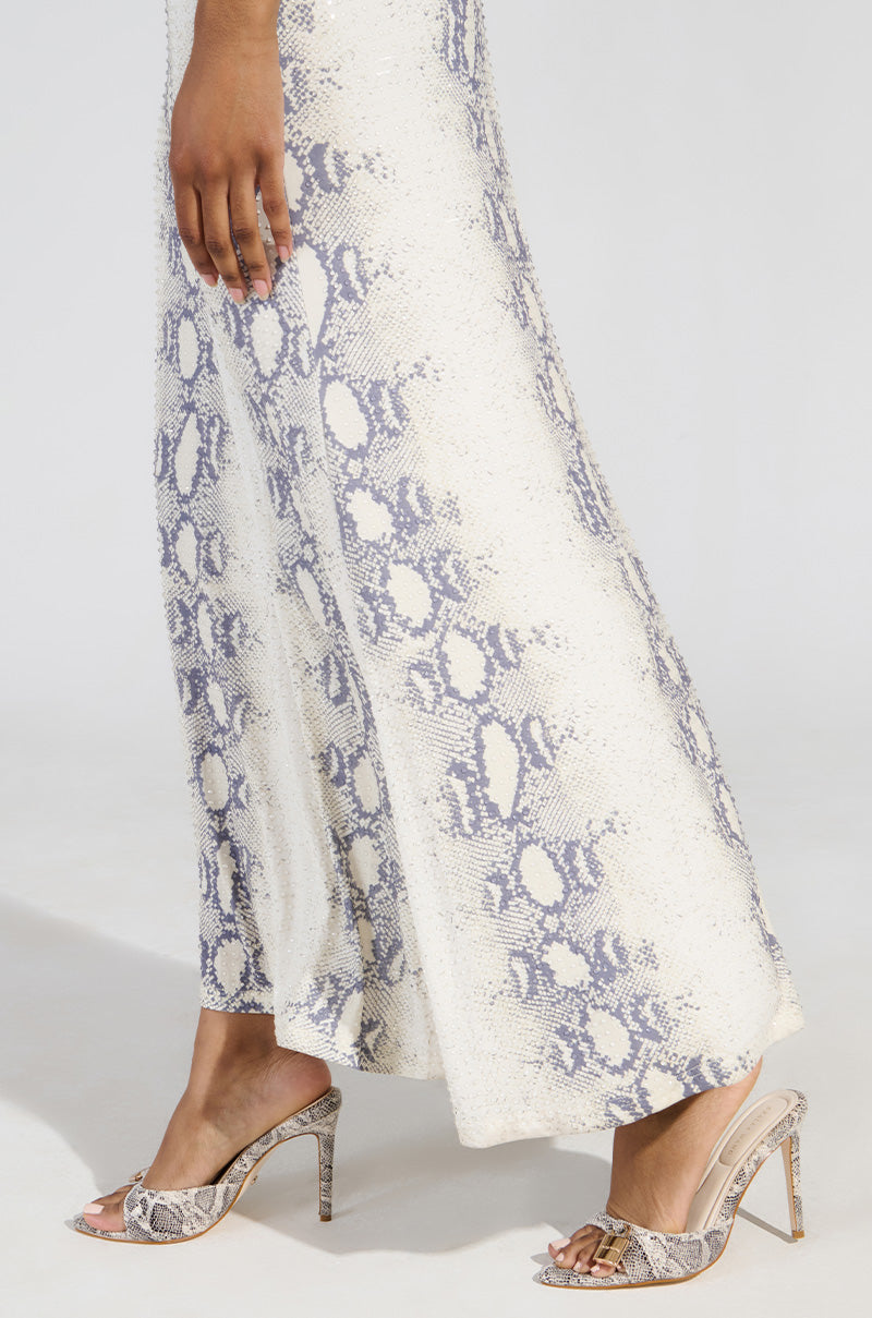 Someone is wearing a long white and gray snakeskin-patterned skirt paired with AZALEA WANG CHUG SNAKE SANDAL, featuring a striking print and gold buckle detail against the plain white background.