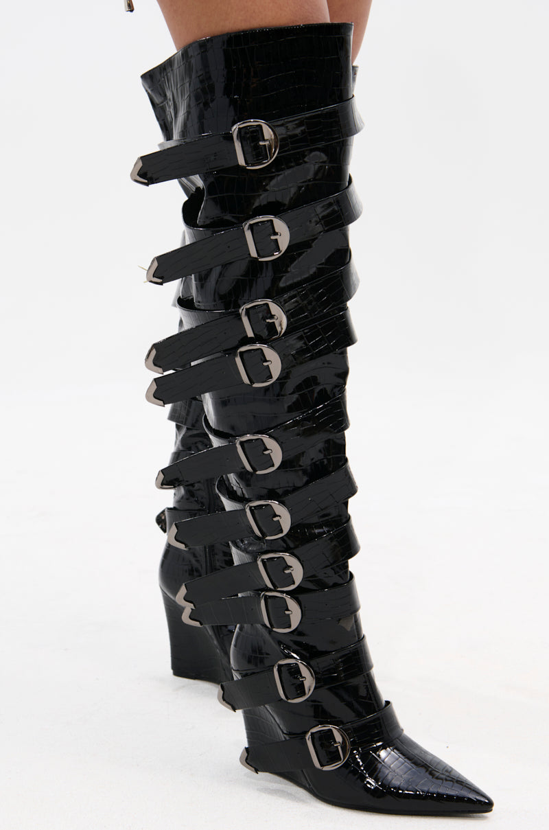 The AZALEA WANG CINZIA BLACK CROC BUCKLE WEDGE BOOT is a knee-high, faux patent leather boot with a pointed toe and multiple wide straps with large silver buckles.