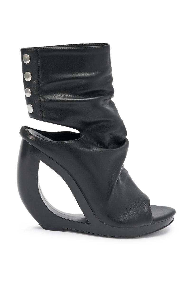 The AZALEA WANG CIRCOS BLACK WEDGE BOOTIE features a modern design with a curved wedge heel, open toe, cutout side, and silver button details at the ankle.