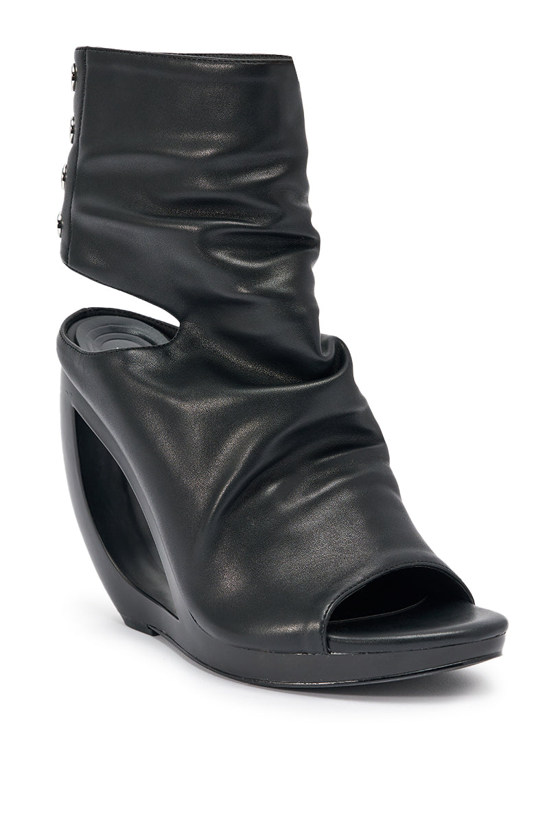 The AZALEA WANG CIRCOS BLACK WEDGE BOOTIE is a black, high-fashion peep-toe ankle boot with a curved wedge heel, ruched leather upper, and decorative back buttons.